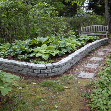 curved and straight rock lock assembled to make garden bed with plants inside along a pathway