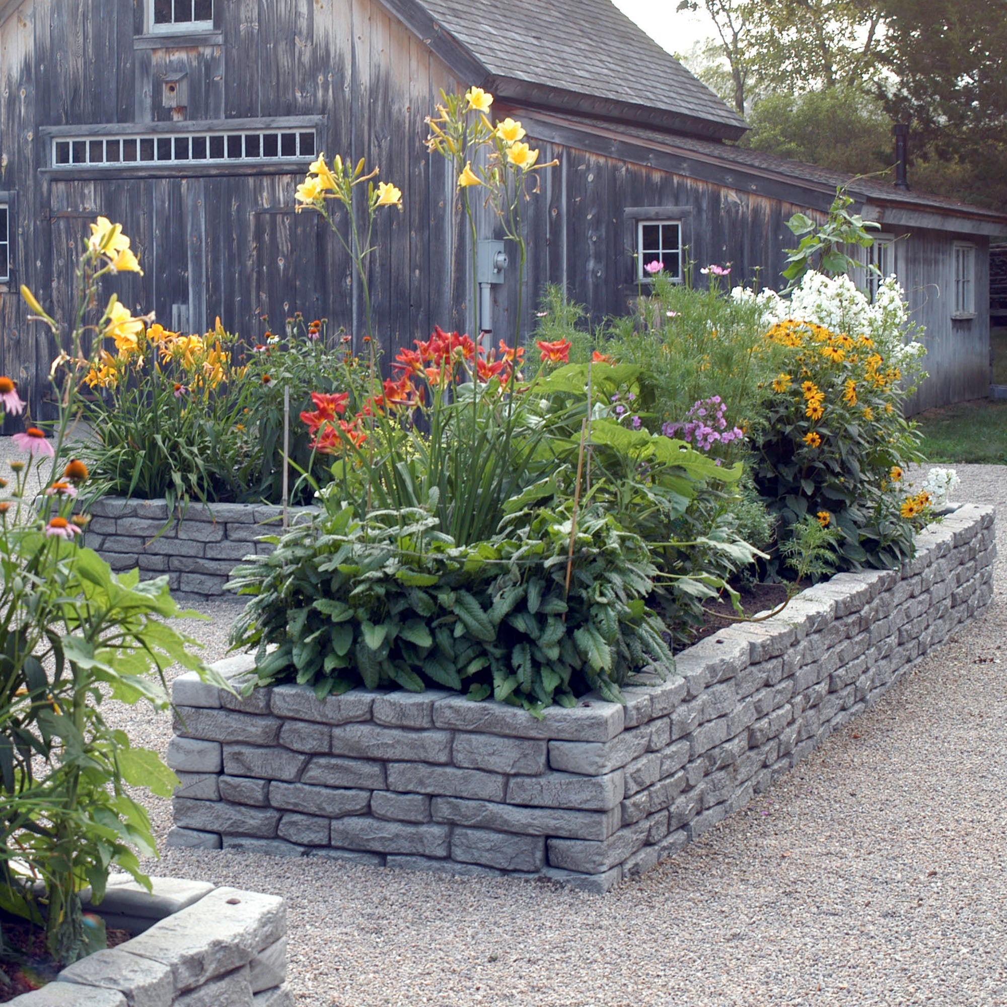 Straight rock lock assembled two high to create garden bed with flowers inside and barn in background