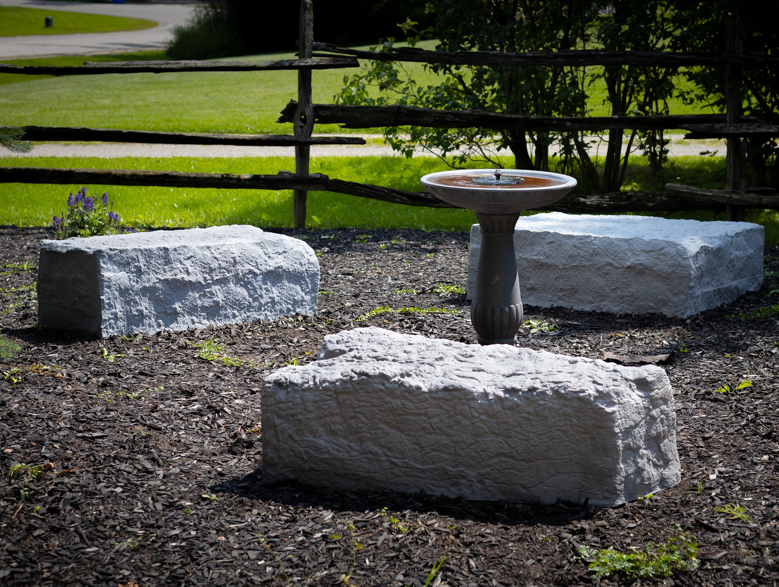 extra large, large and triangle landscape rock in grey on a woodchip garden with bird bath in the middle and wooden fence in background